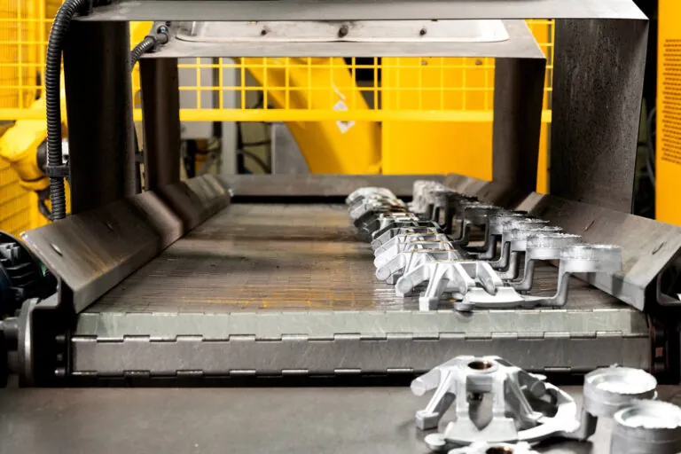Freshly cast aluminum components on an automated conveyor system after high-pressure die casting and robotic trimming.